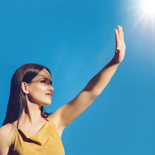 Woman shielding her eyes from bright sunlight with her hand, highlighting the impact of UVA and UVB rays on eye health.