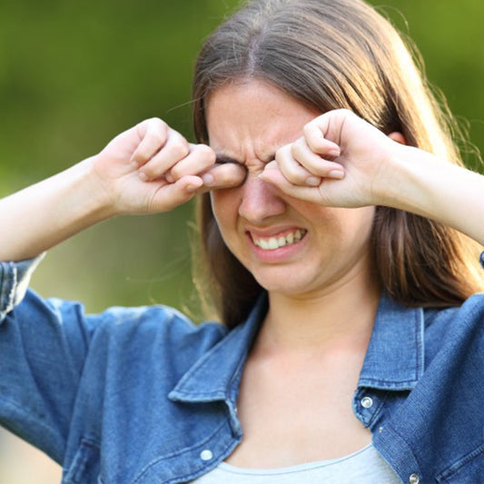 Young woman outdoors rubbing her eyes due to irritation caused by dry weather and environmental factors affecting eye health.