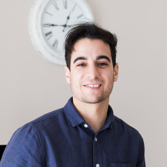 Man wearing a blue shirt with a clock in the background.